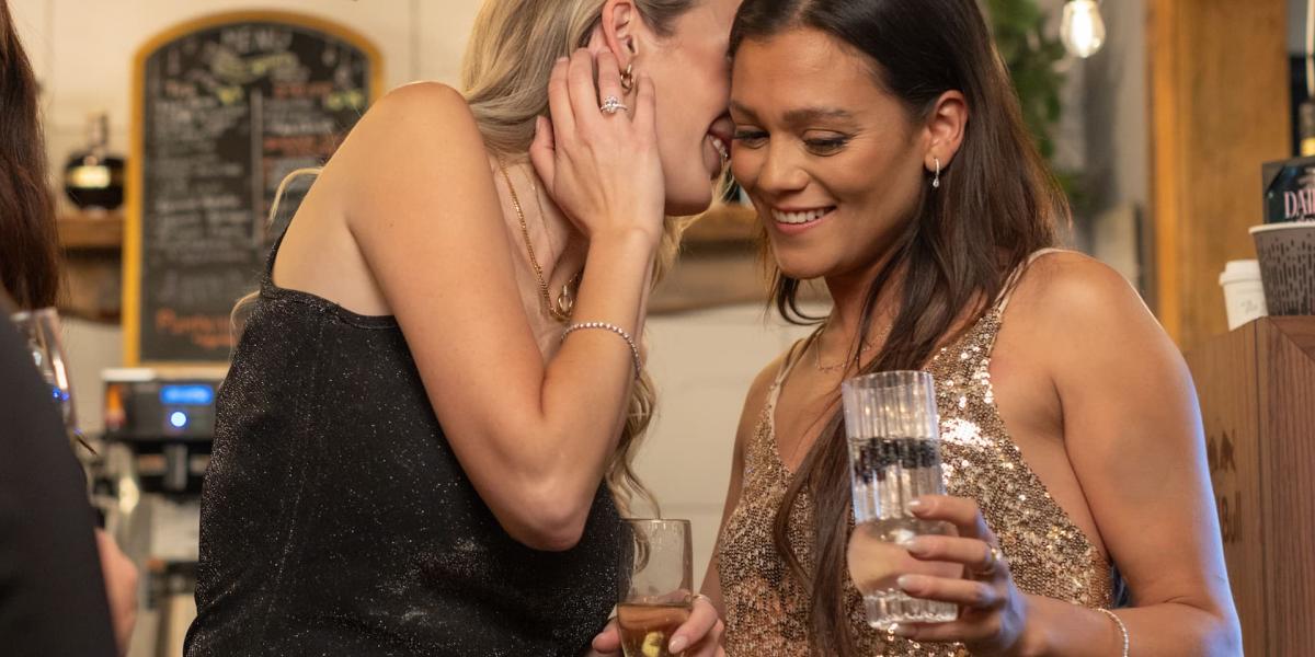 Two women sharing a joyful moment while holding drinks at an elegant evening event